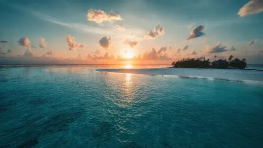 A luxurious, secluded island resort with pristine beaches and clear blue waters, but with a subtle, ominous undertone, hinting at hidden darkness. The sun is setting, casting long shadows.