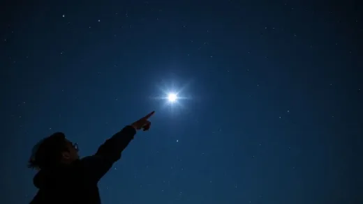A person pointing at a bright star in a clear night sky, surrounded by other stars and a faint Milky Way, with a sense of wonder and discovery.