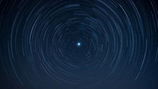 A clear night sky with stars trailing in circular paths around a stationary, bright Polaris, seen from the Northern Hemisphere, showing Earth's rotation effect.