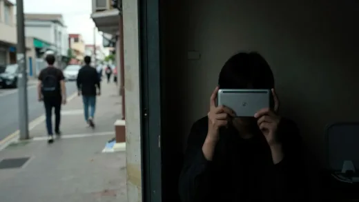 A split image: one side shows a seemingly ordinary street with people walking by, the other side shows a dimly lit room with a person discreetly hiding a modern device or a forbidden item, reflecting a dual life.