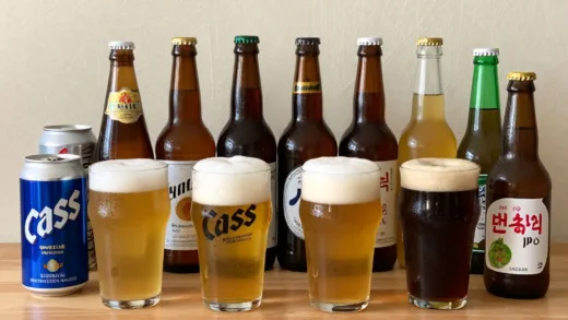 A visually appealing spread of various craft beers and popular Korean and Japanese beers, with some foam art. Include brands like Cass, Suntory Premium Malt, and Weihenstephaner. Soft, inviting lighting, creating a cozy atmosphere.