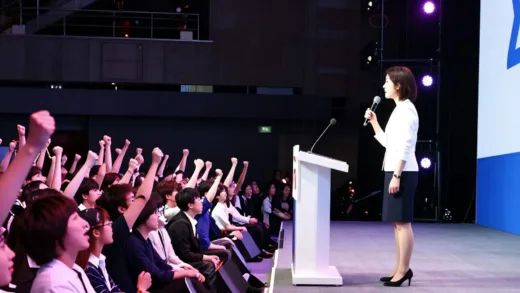 A dynamic, modern political rally in Japan with many young people cheering, a female politician on stage, vibrant lights, and a sense of excitement.