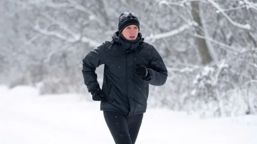 A person running outdoors in cold winter, looking uncomfortable and bundled up. The background is a snowy, windy landscape.