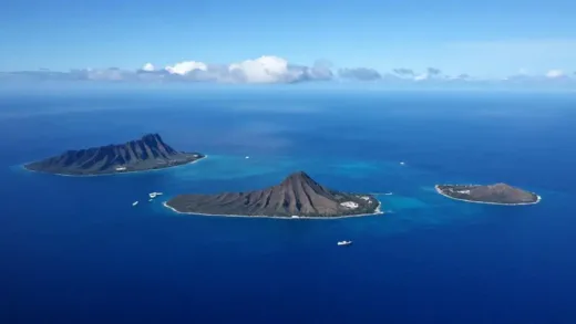 A stunning aerial view of Hawaii's main islands (Oahu, Maui, Big Island, Kauai) in deep blue Pacific Ocean, with no visible ferries connecting them. A sense of beautiful isolation and mystery. Clear sunny day with scattered clouds. High resolution and vivid colors.