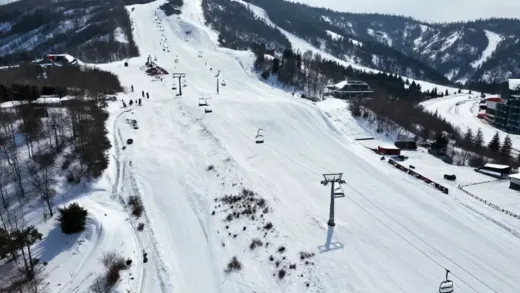 An aerial view of a once bustling ski resort with long lines for lifts and crowded slopes, contrasted with a present-day image of the same resort looking desolate, with overgrown weeds on the slopes and empty chairlifts. Winter season, snowy mountain, bright daylight.