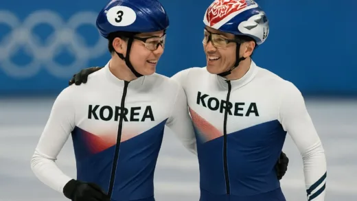 Two Korean short track speed skaters, one young and one experienced, standing together on the ice rink at the Winter Olympics, wearing team Korea uniforms, smiling and looking at each other with mutual respect, in a dynamic sports photography style with focus on their interaction