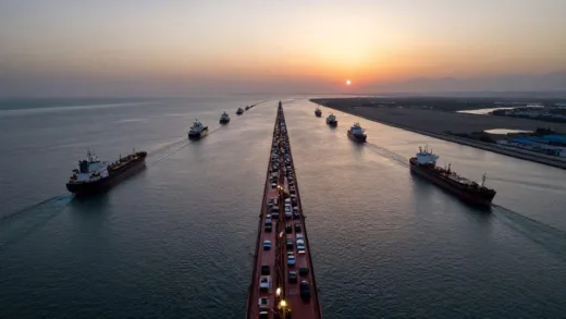A dramatic aerial view of the Strait of Hormuz with numerous oil tankers backed up in a traffic jam, showing the narrow waterway between Iran and Oman, at sunset