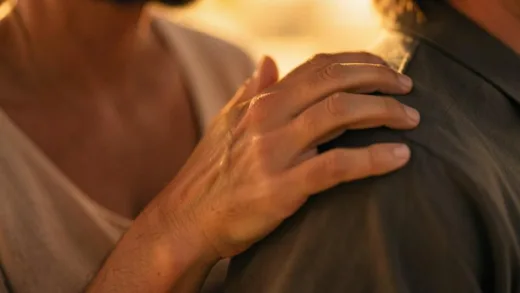 A close-up shot of a hand gently touching another person's shoulder in a warm empathetic gesture, soft lighting, warm colors, cinematic composition