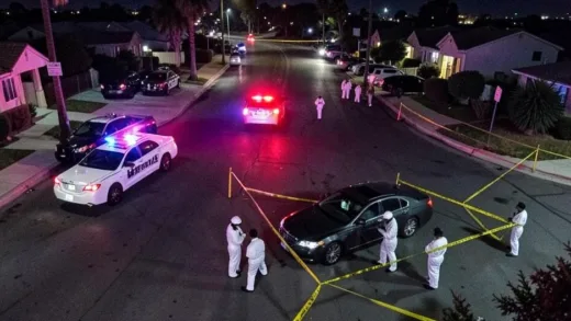 Aerial night view of a crime scene in Los Angeles with police vehicles, yellow caution tape around a parked luxury car, forensic investigators in white suits, and flashing red and blue lights illuminating the suburban street