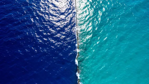 A split view of two different colored ocean waters meeting with a visible boundary line, dramatic aerial photography style, deep blue and turquoise waters contrasting, sunlight reflecting on the surface