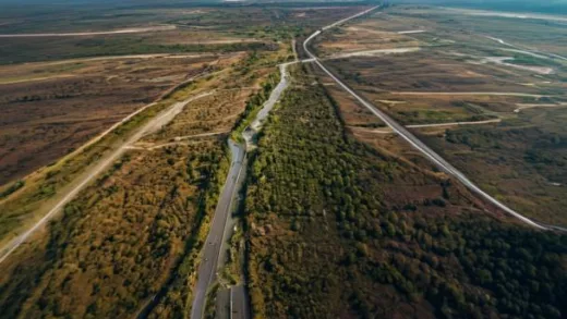 An aerial satellite view showing a newly constructed wide tactical road cutting through a deforested area in the demilitarized zone, leading close to a visible border line, with a sense of tension.