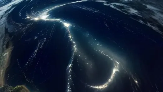 NASA-style night satellite image of the eastern United States, glowing city lights forming a bright corridor along the northeast coast from Boston to Washington DC, bright Florida peninsula, and a notably dark empty stretch of coastline along Georgia and the Carolinas, deep blue ocean with subtle clouds, high resolution earth observation photography